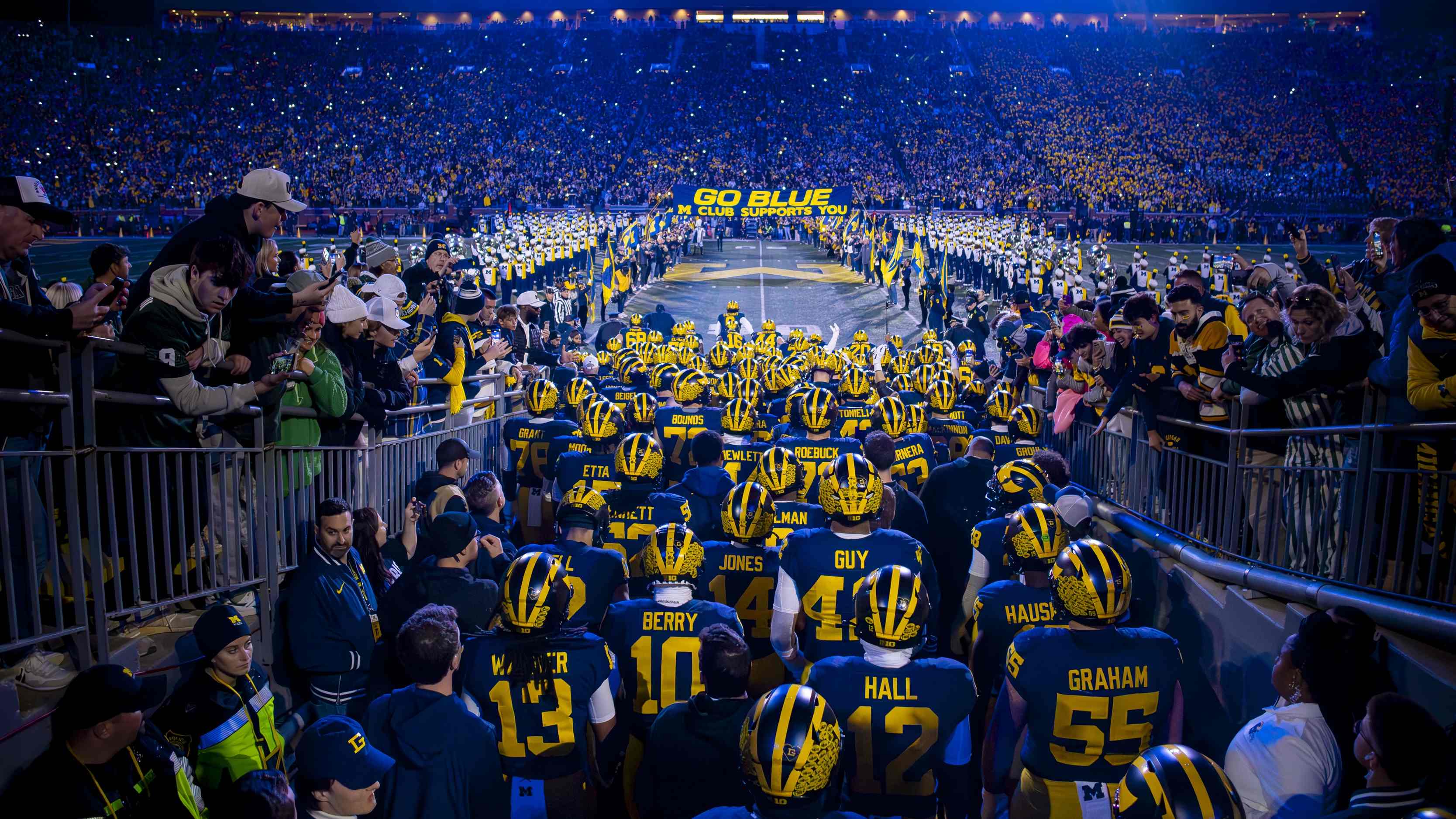 The U-M football team, seen from behind, coming out of the tunnel at Michigan Stadium, in maize and blue uniforms