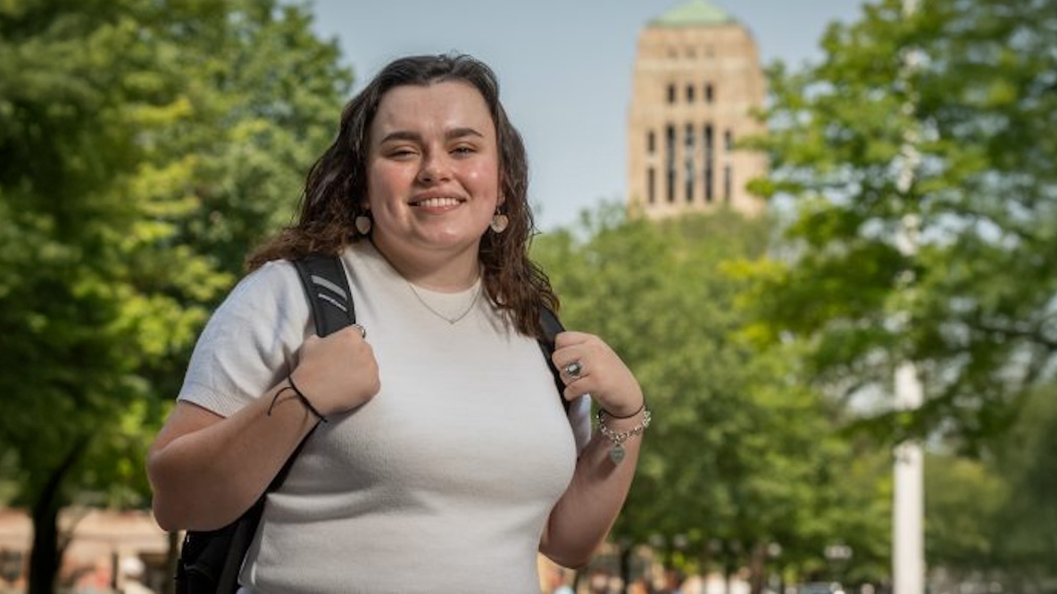 Woman in a white t-shirt with trees and the U-M Bell Tower in the background.