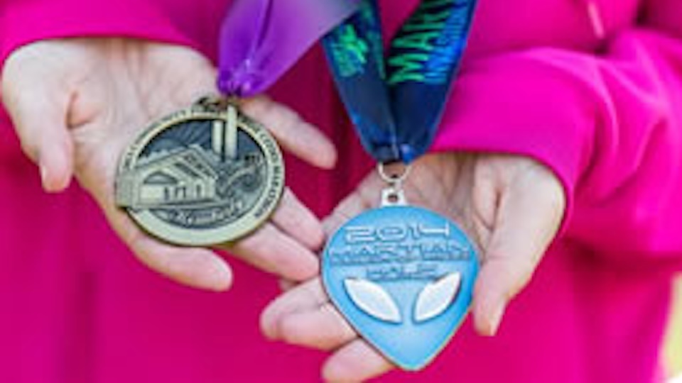 A woman’s hands holding out two medals that drape from around her neck.