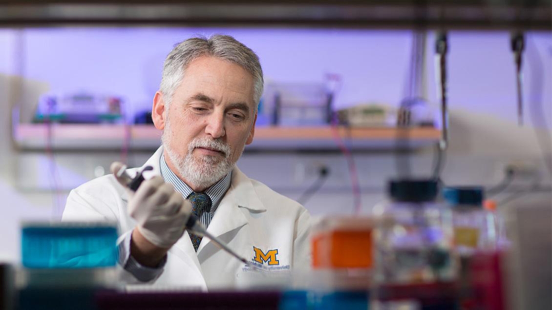 A man in a lab coat with a U-M Block M on it in a laboratory