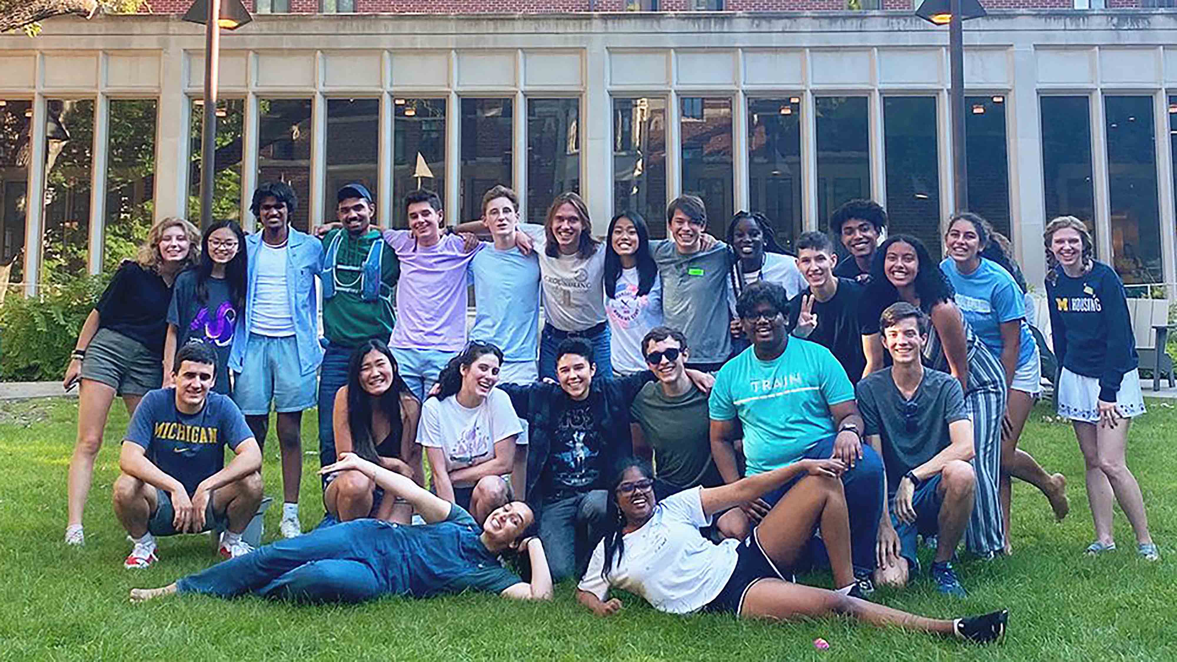 A group of students gathers outside on a grassy area in front of a large building