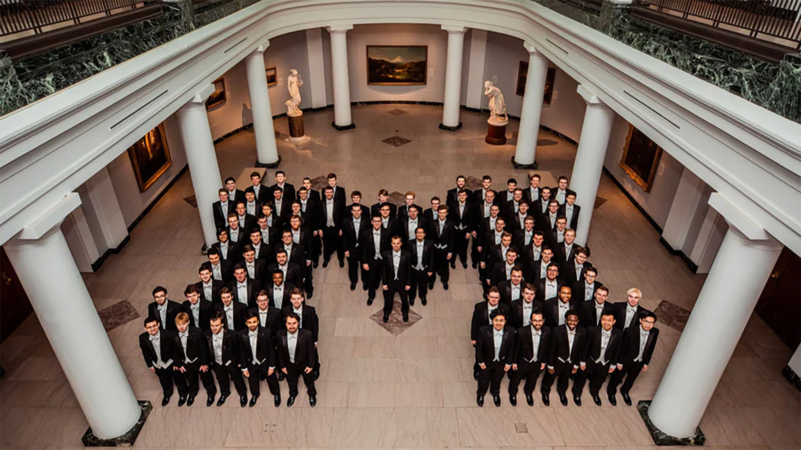 A group of men in tuxedos, in the form of an M