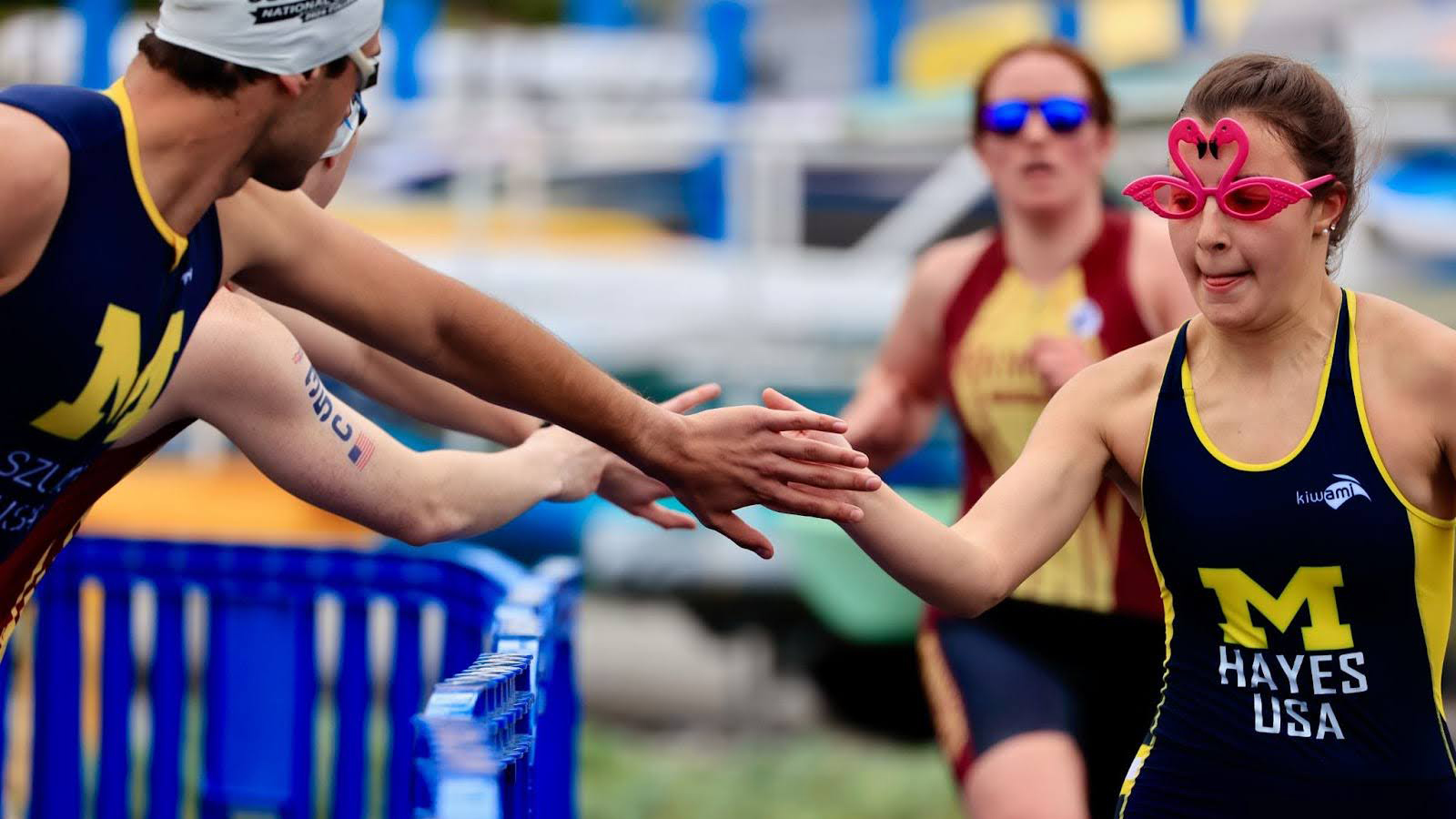 Two athletes in University of Michigan uniforms reach toward each other for a high five.