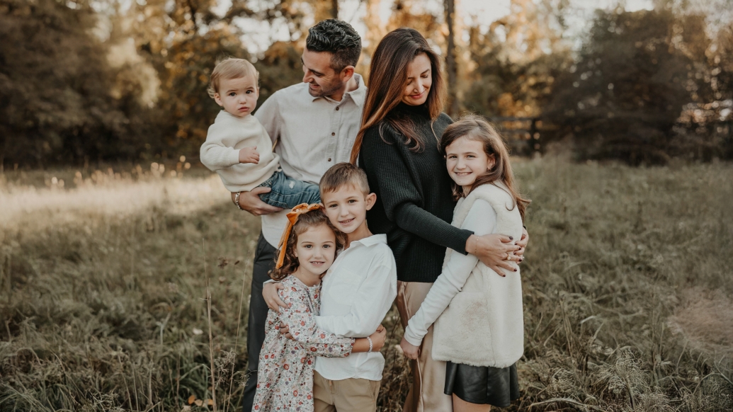 Mom, dad and four kids outside in field with trees behind