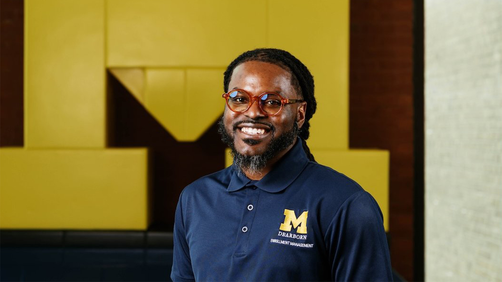 Kevin Towns standing in front of a Block M mural wearing a UM-Dearborn shirt.