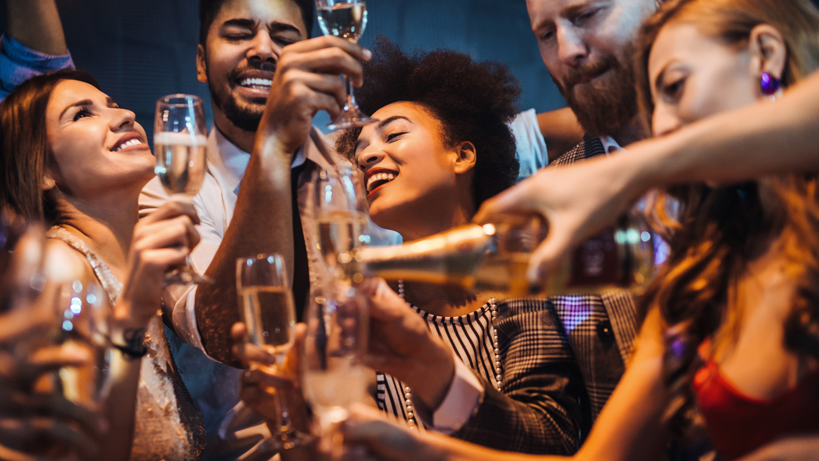 Several people hold up champagne glasses as a bottle is being poured.