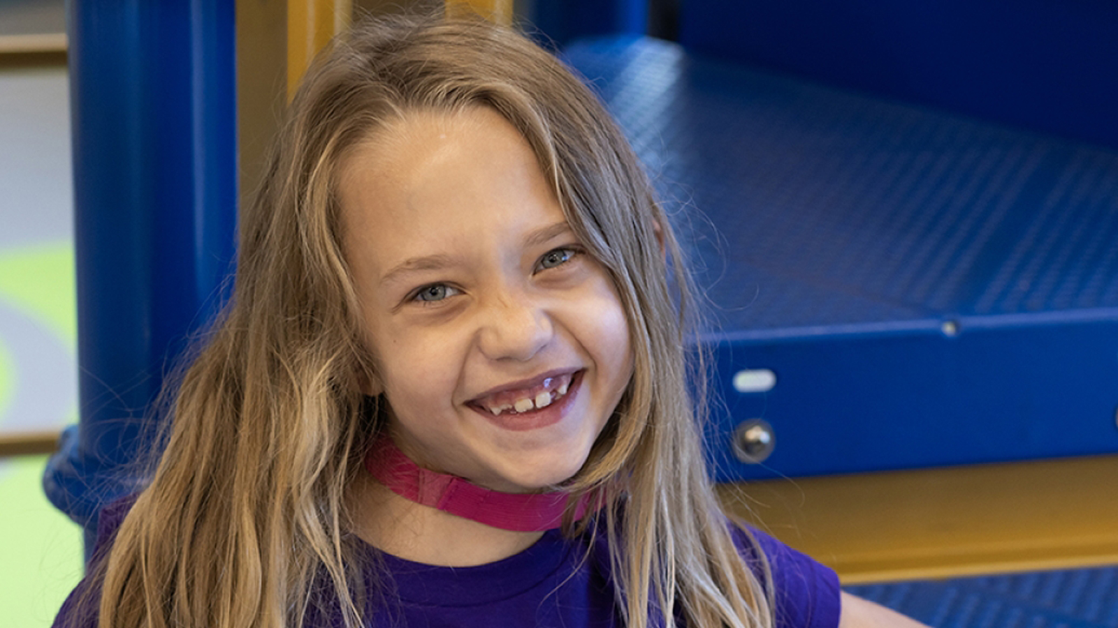 A young child with long blonde hair and a purple shirt at a playground.