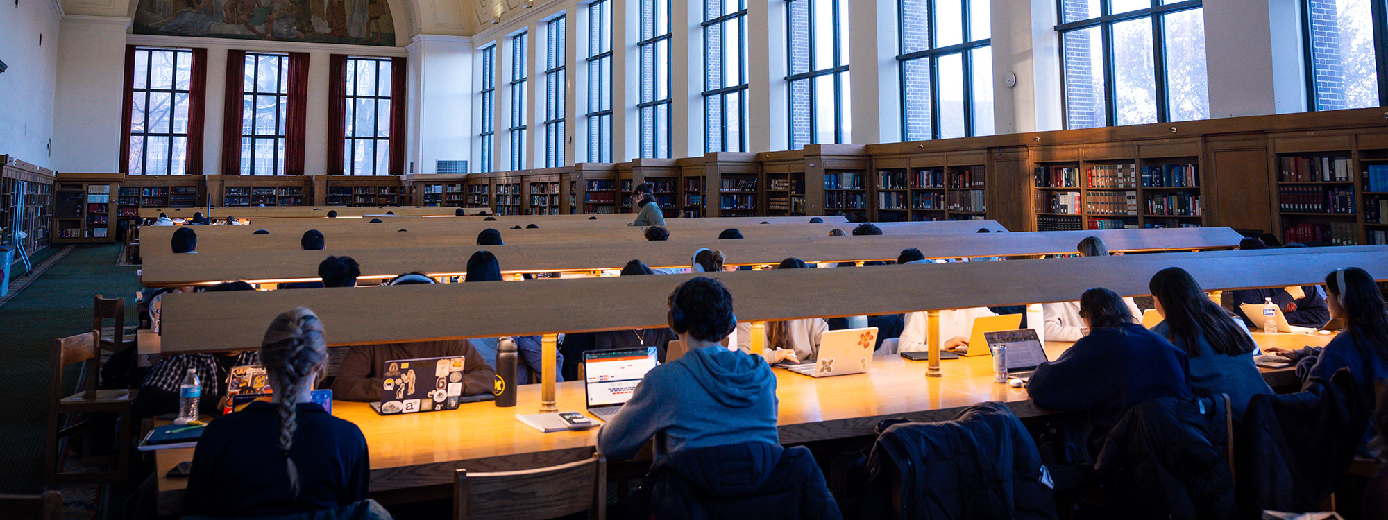 Students study at long wooden tables under bright lights in a Michigan study hall.