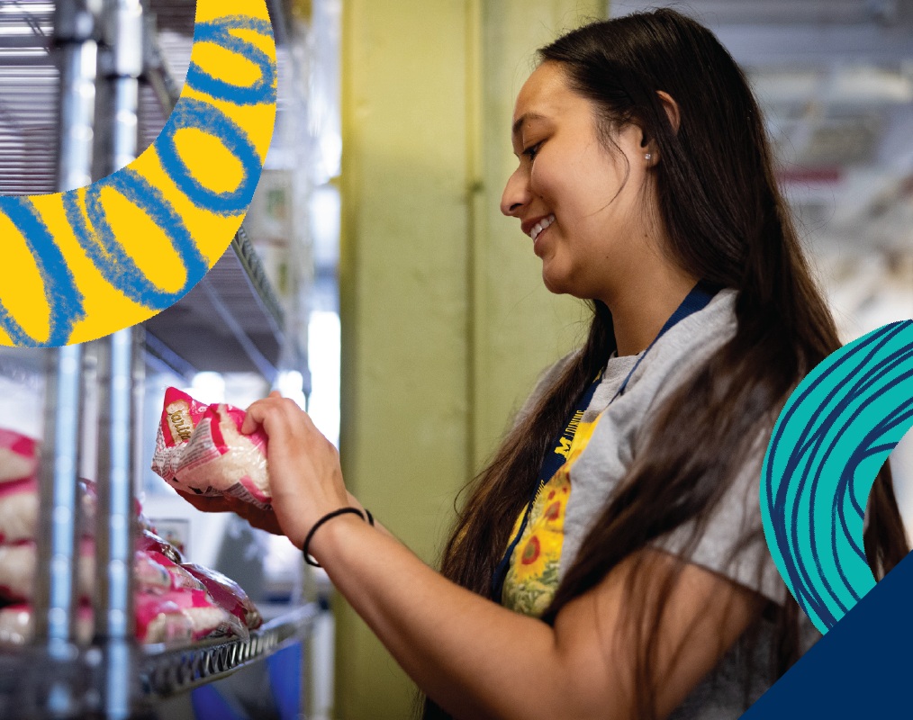 A smiling University of Michigan student getting groceries from the Maize and Blue Cupboard.
