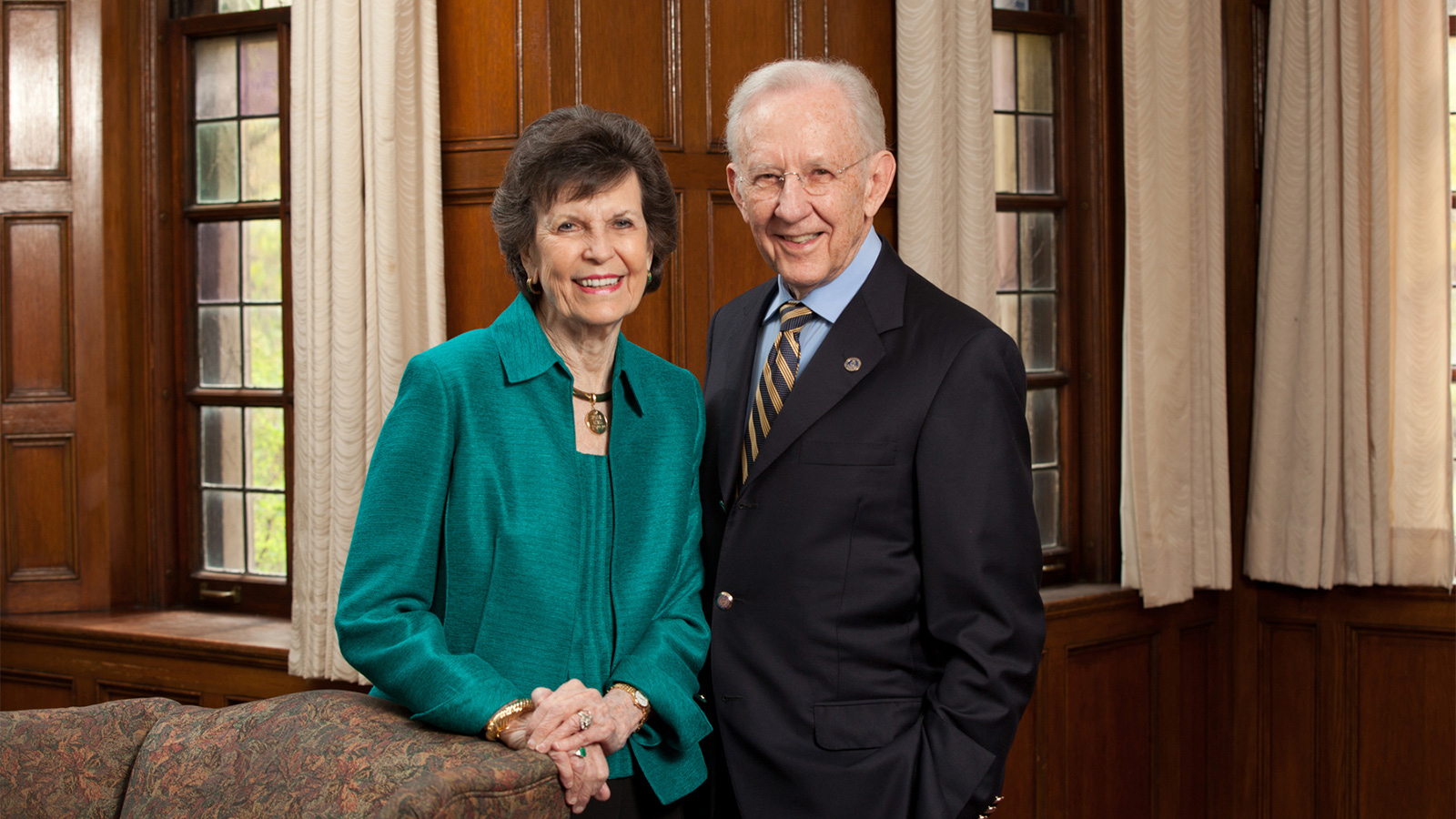 Delores and William Brehm posing for a portrait photo in a room with wooden walls and windows in the background.