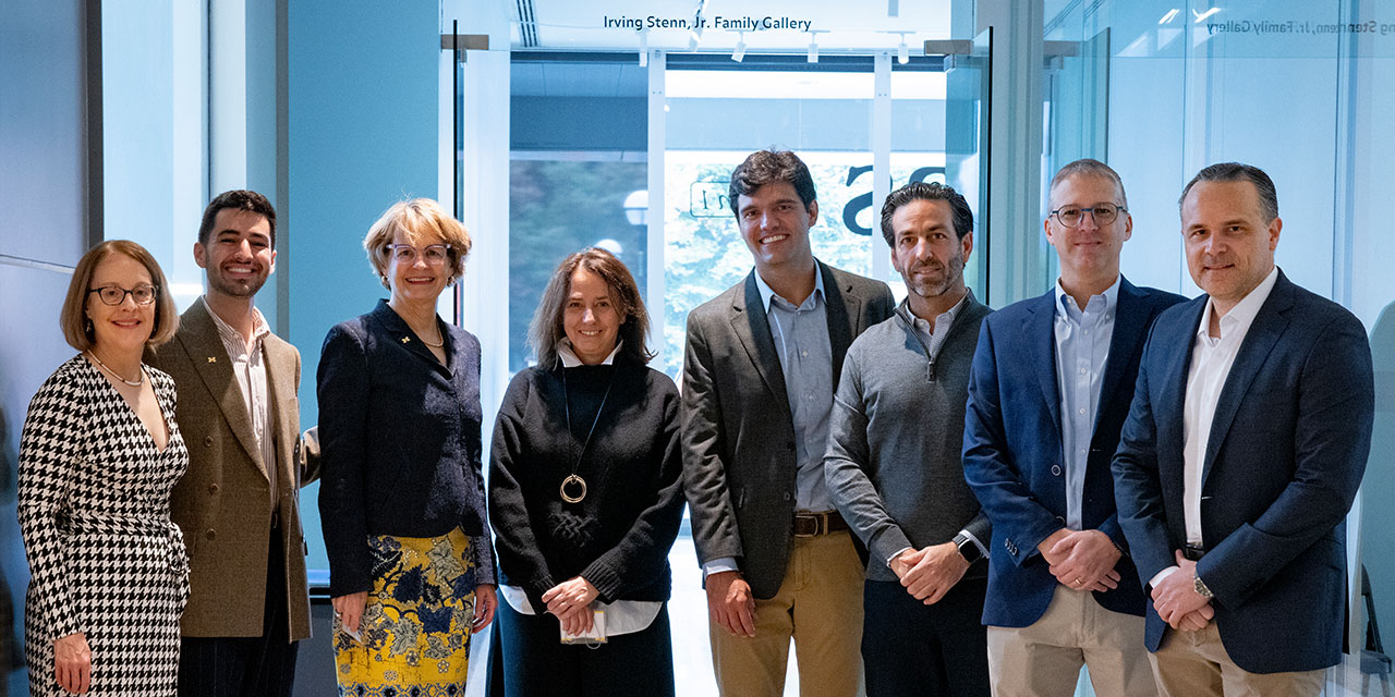 Eight adults standing side by side in a brightly lit gallery room.