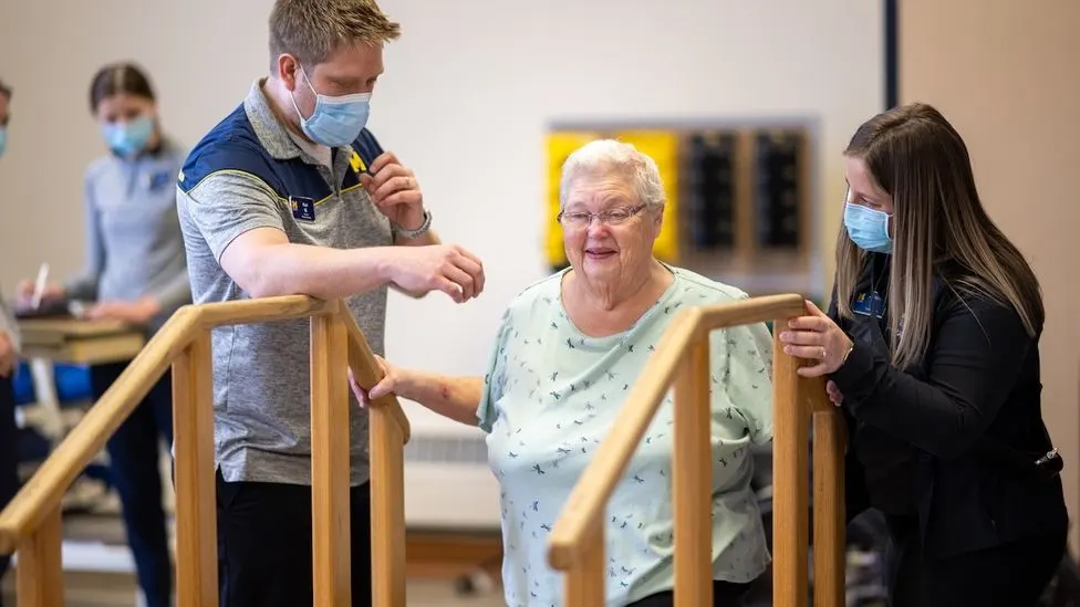Two staffers at the HEART Clinic helping a patient climb stairs.