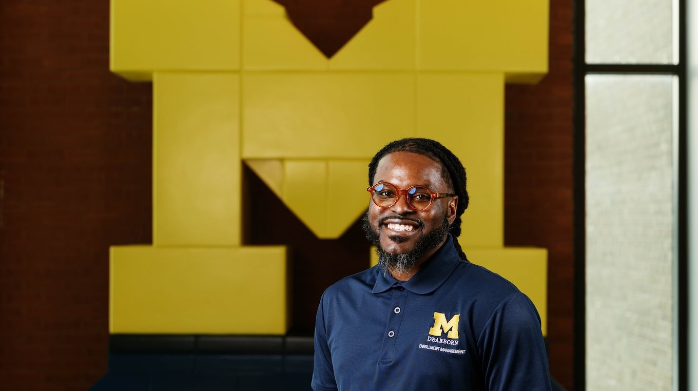 Kevin Towns standing in front of a Block M mural wearing a UM-Dearborn shirt.