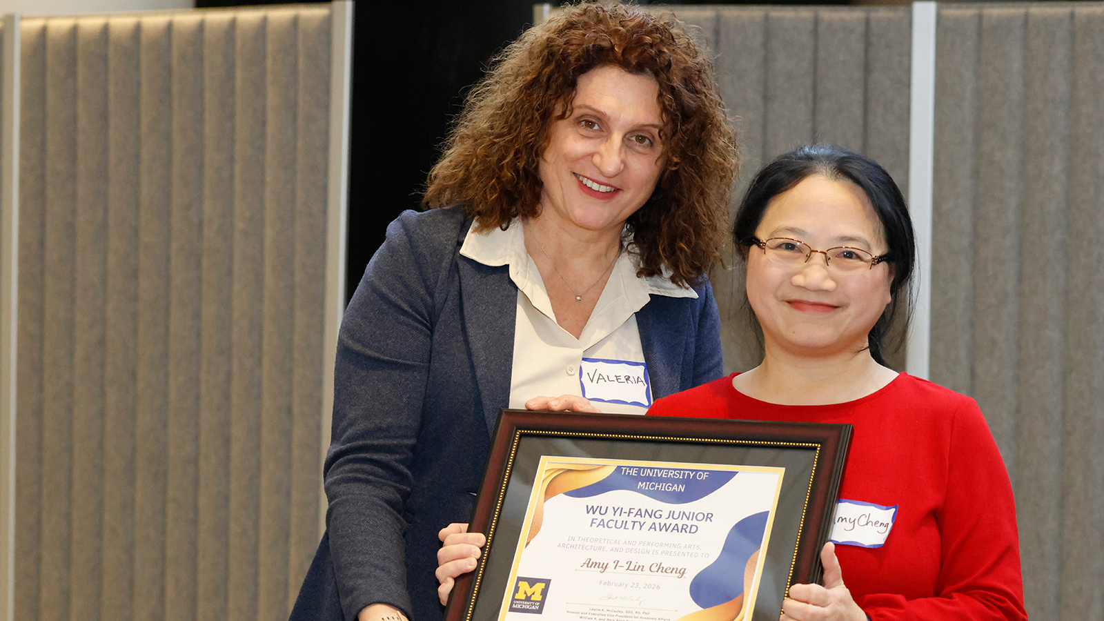 Two people pose together holding a framed University of Michigan award certificate.