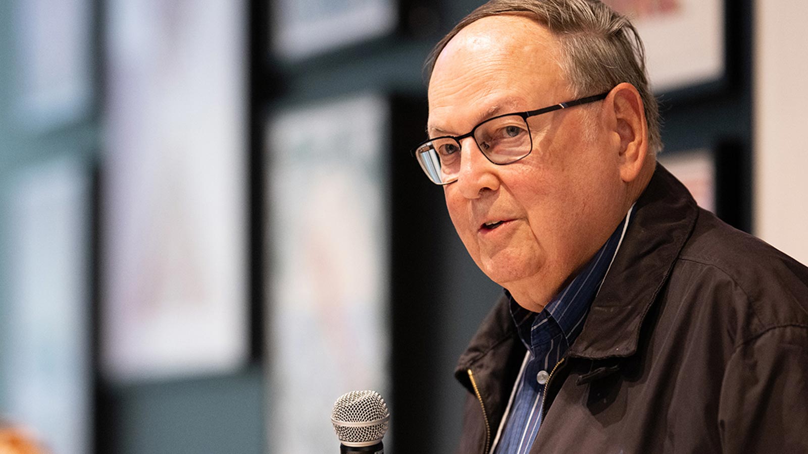 William Weese holds a microphone while speaking indoors.