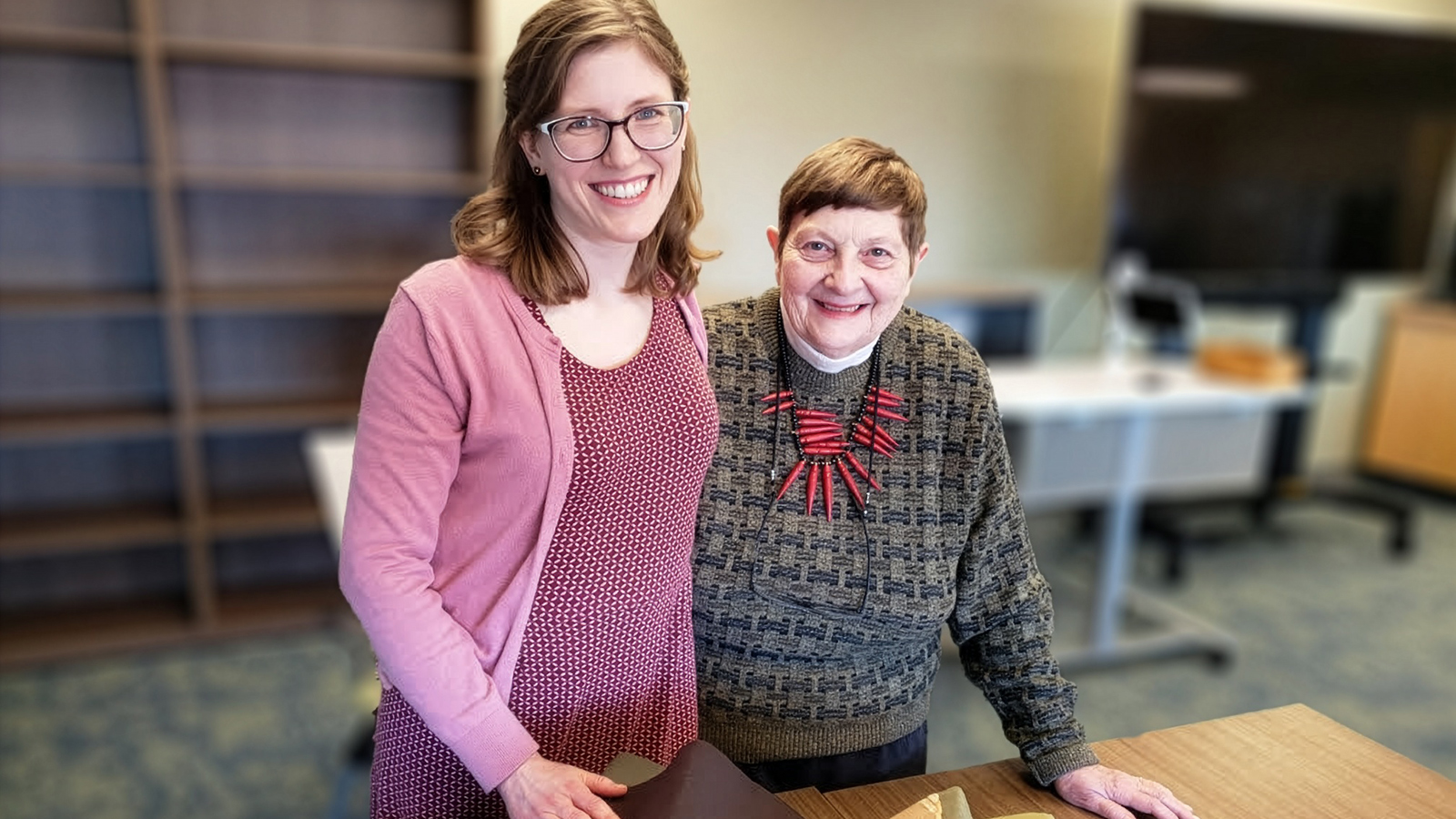 Juli McLoone, curator in the Special Collections Research Center, and Janice Longone stand beside an open archival book on a table in the University of Michigan Library.