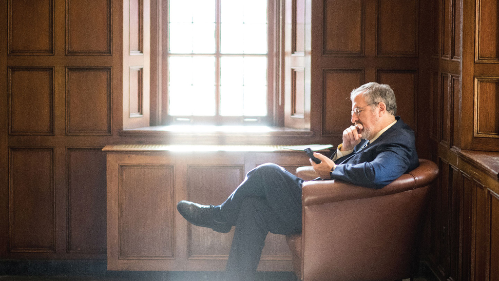 President Mark Schlissel sitting in a chair and looking at a phone.