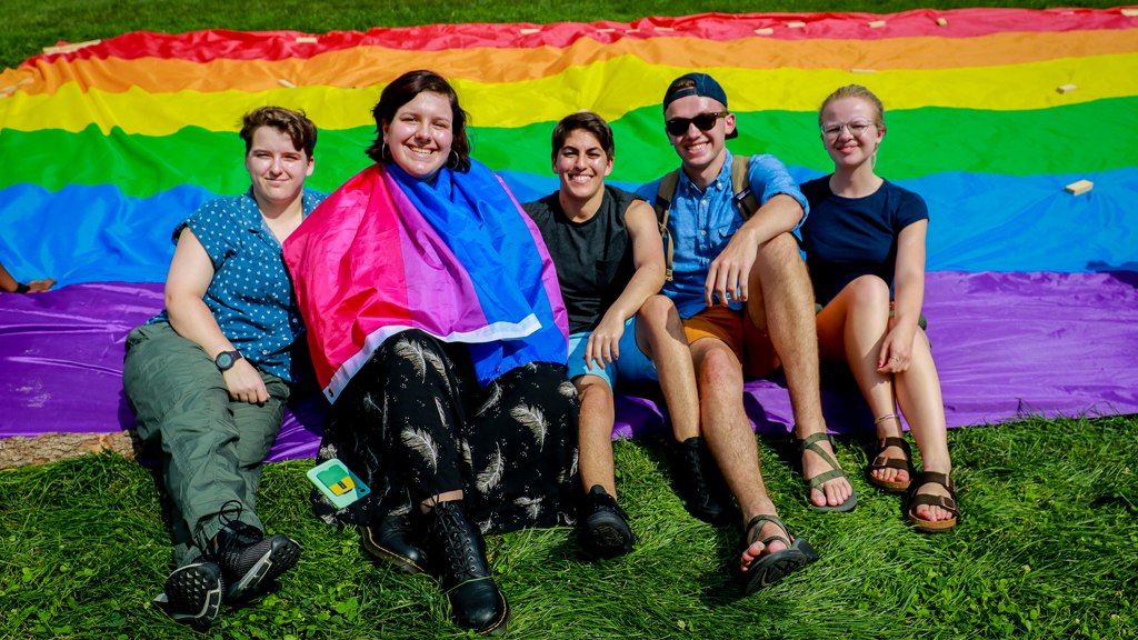 Students sitting outside in front of a Pride flag.
