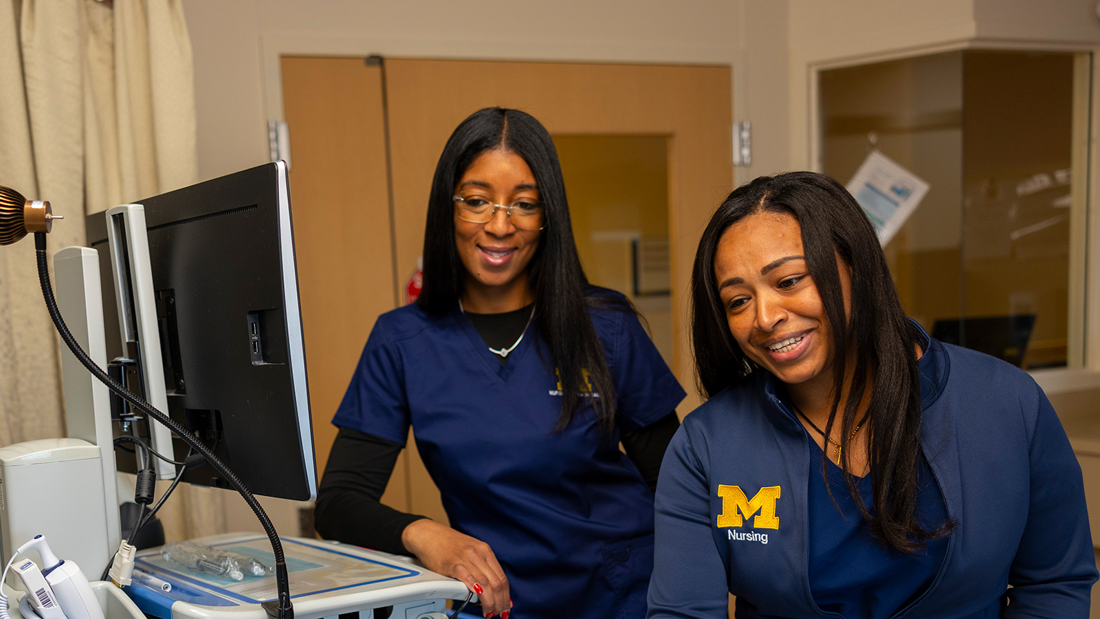 Two Michigan Medicine nurses smiling while looking at a medical monitor.