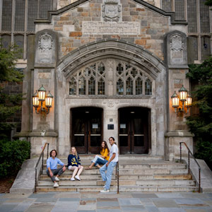 Four people sitting on the steps outside the William W. Cook Legal Research Building’s ornate entrance.