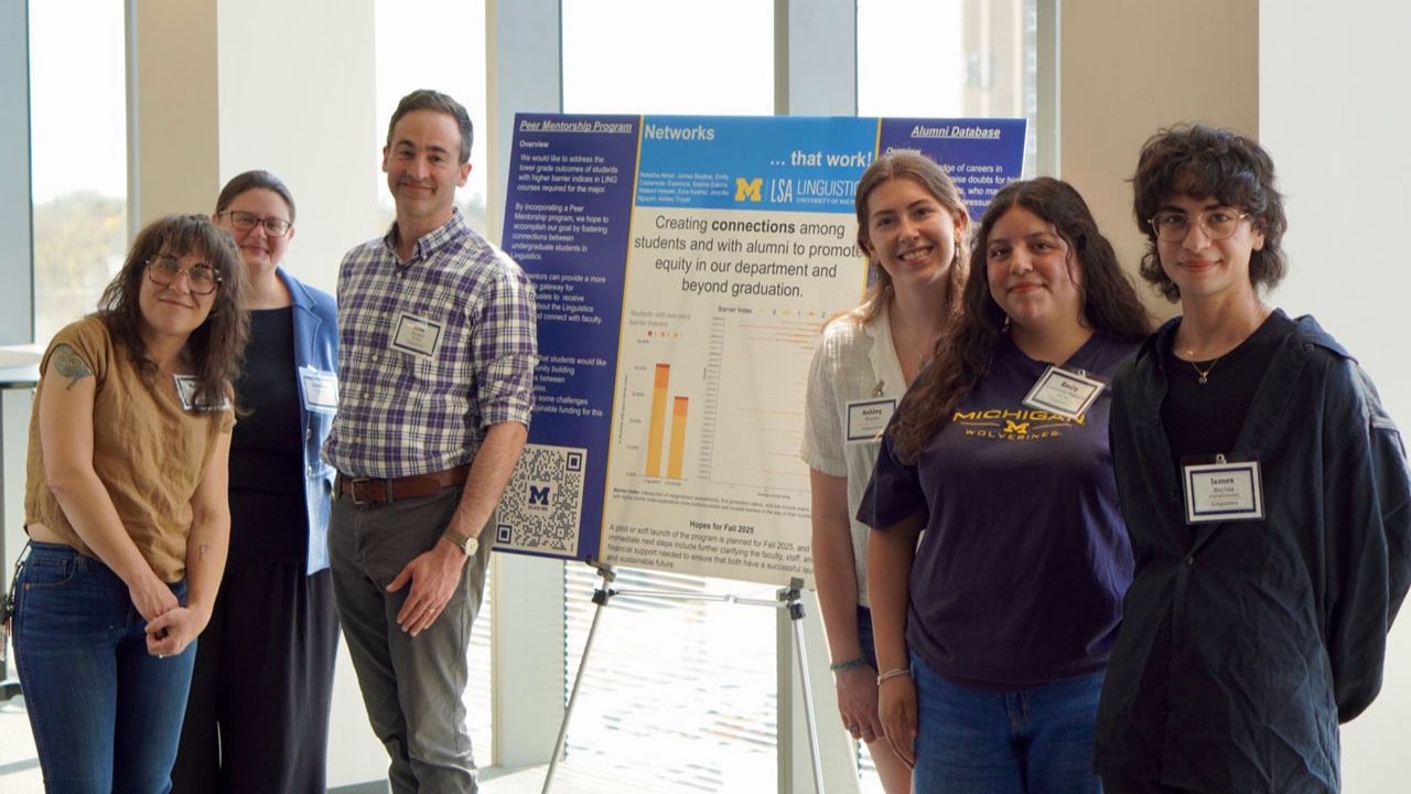 Six people pose beside a University of Michigan Linguistics poster about a peer mentorship program connecting students and alumni.