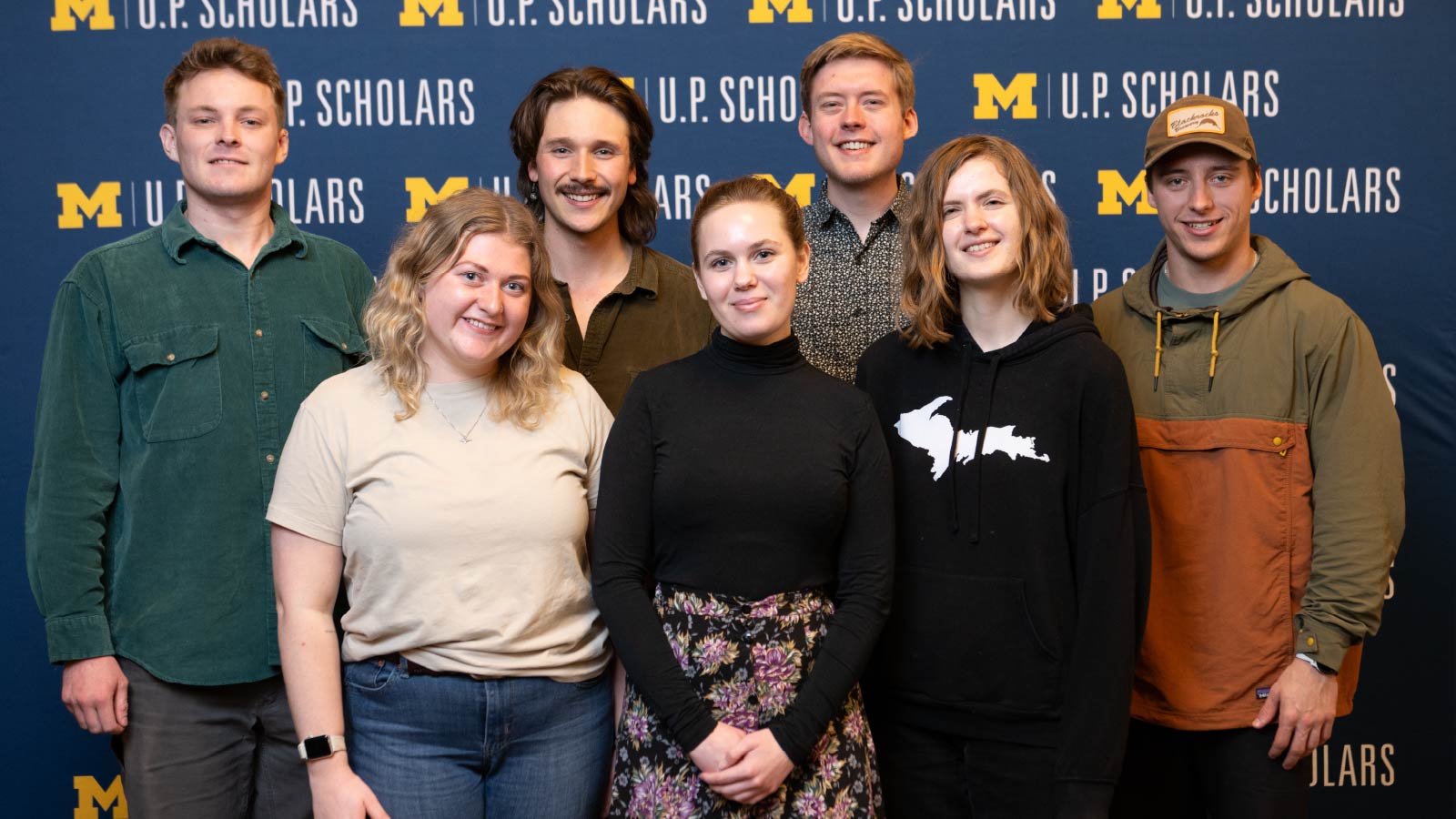 Seven members of the U.P. Scholars 2024 cohort standing in front of a banner that reads “U.P. Scholars”