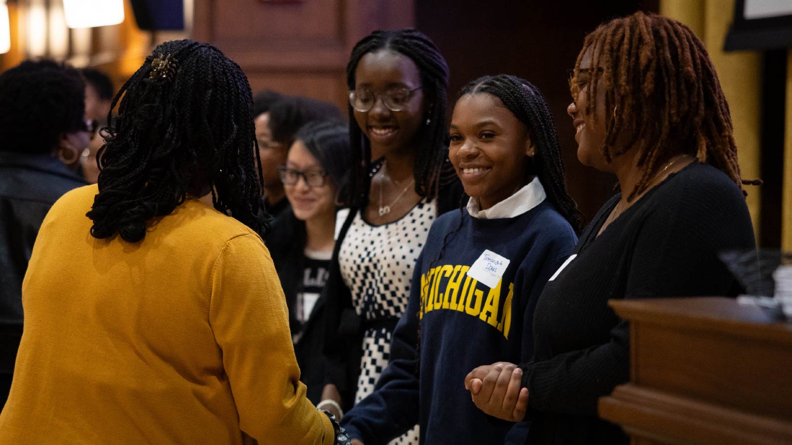 A few students in a group smiling and one is shaking hands with a woman.