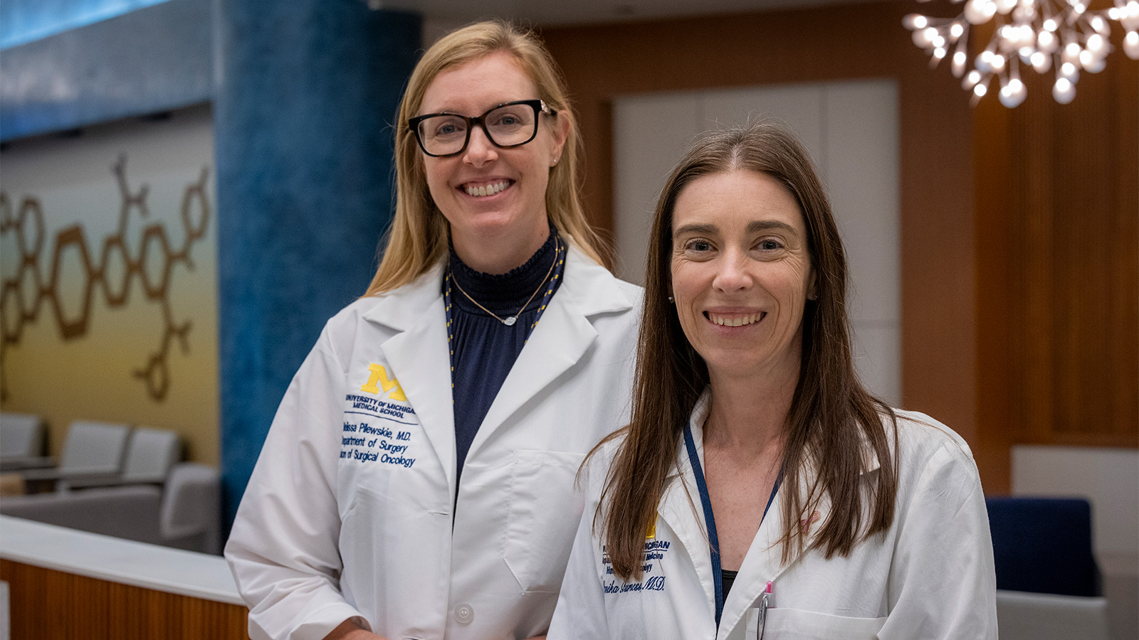 Two women in lab coats standing next to each other. 