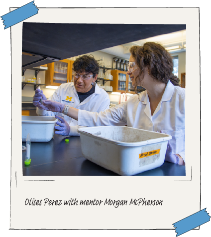 Aspirnaut student Olises Perez and mentor Morgan McPherson, both wearing lab coats, work together at a table in a laboratory