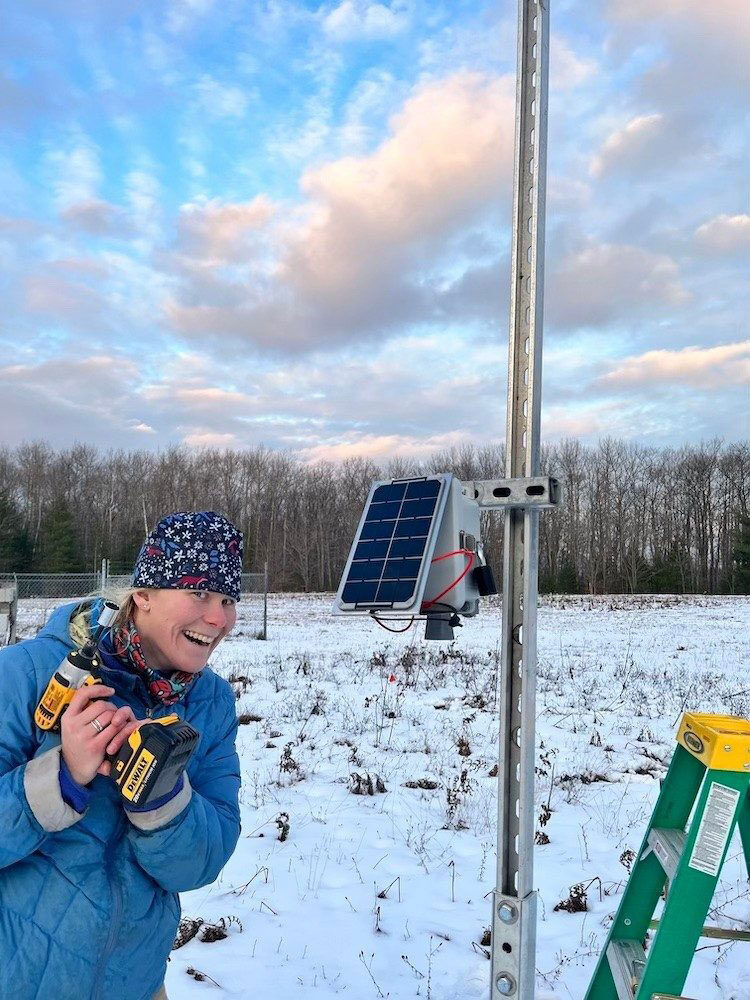 Karin Rand holding a wireless drill and standing by a sensor that measures snowpack