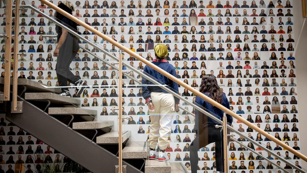 U-M students contemplating a wall of portraits of diverse students.