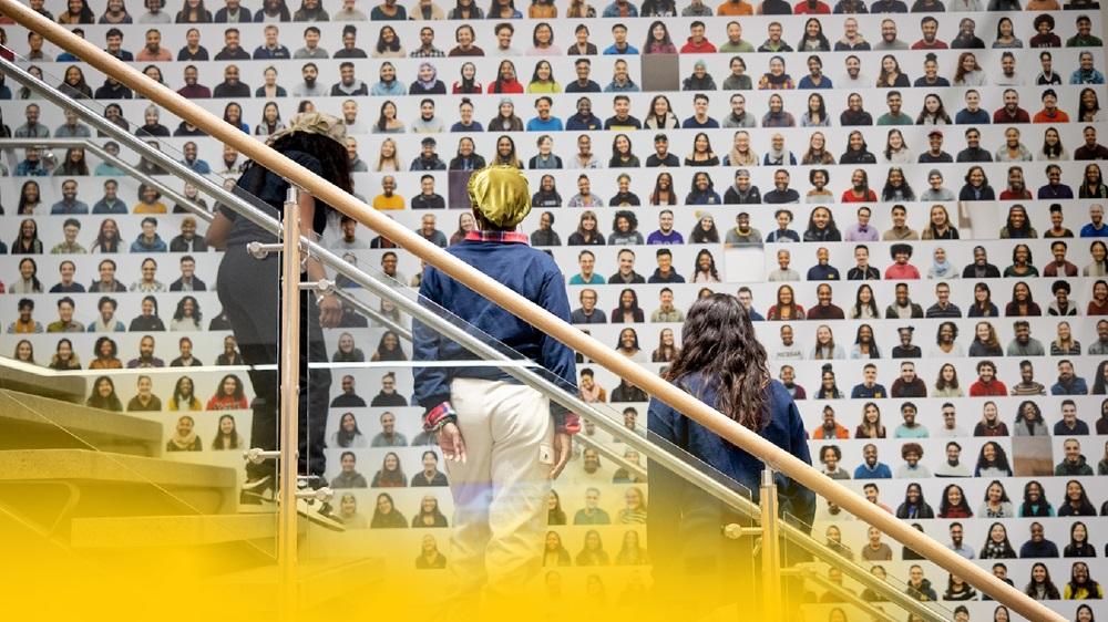 U-M students contemplating a wall of portraits of diverse students.