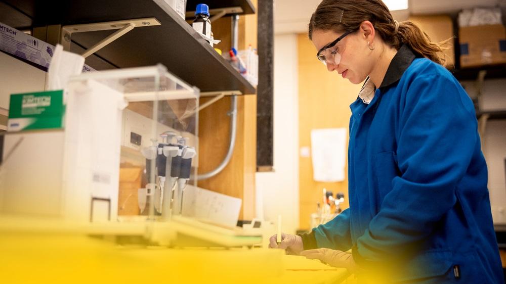 A University of Michigan student in a medical research lab recording experiment results in a notebook.