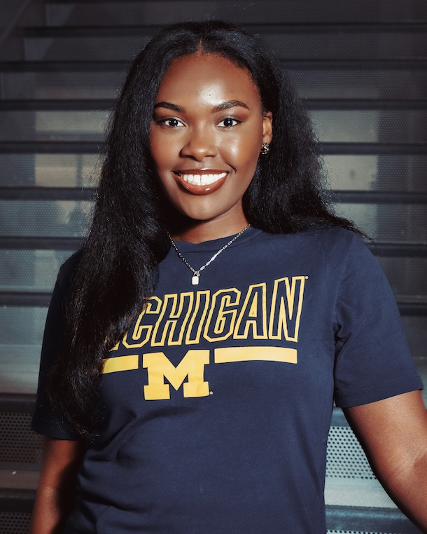 Annesha Hardy smiles, wearing a blue t-shirt with gold University of Michigan Logo