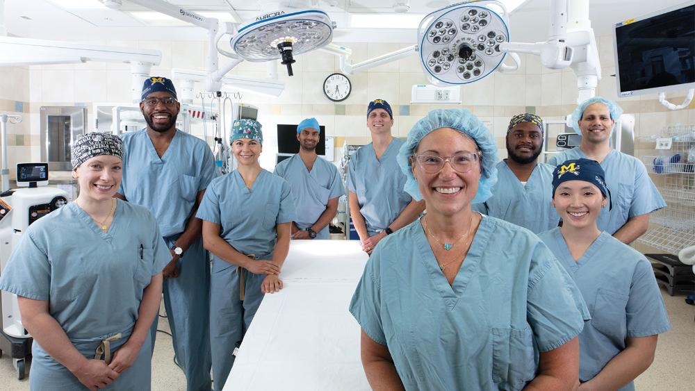 A diverse group of people in medical scrubs and hair nets pose for a photo in an operating room.