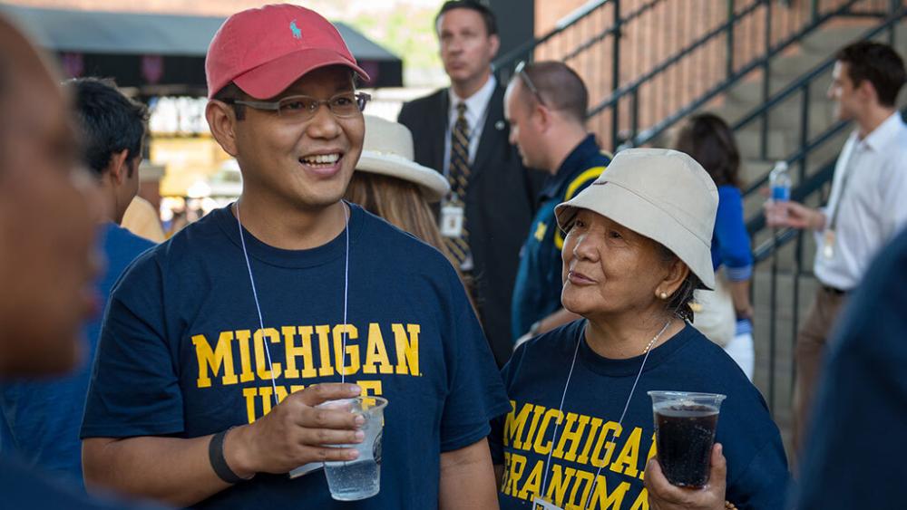 Family of a University of Michigan student talking at a reception. One is wearing a "Michigan Uncle" shirt and the other is wearing a "Michigan Grandma" shirt.