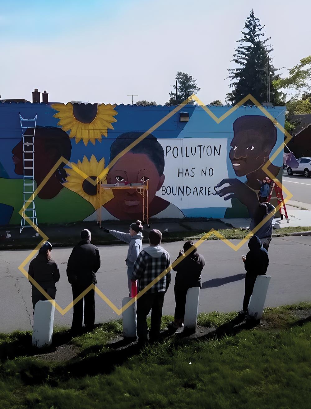 A group of people standing outside across the street from a building with a mural being painted that reads, “Pollution has no boundaries.”