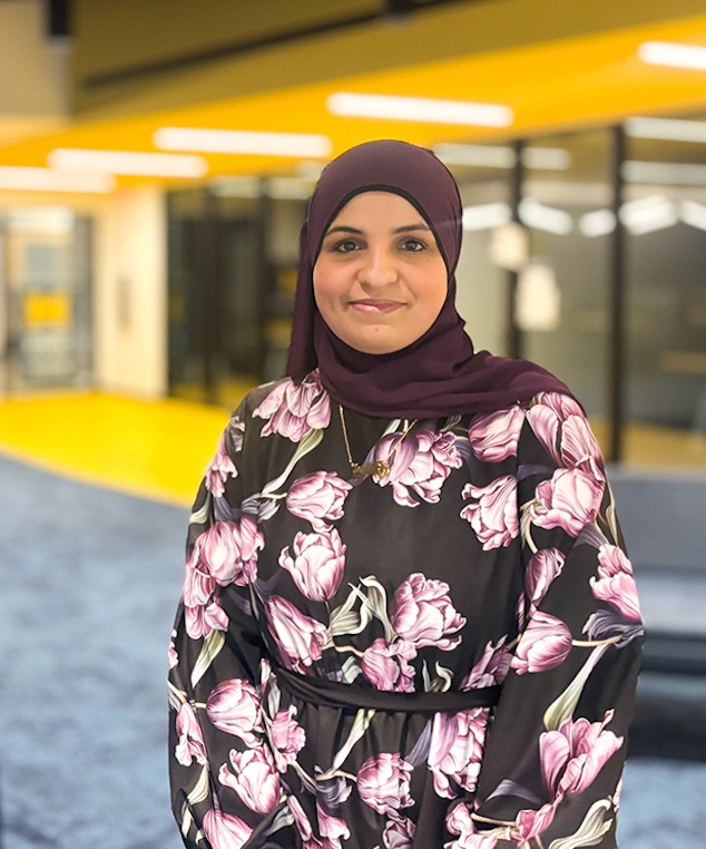 Fatmah Saleh, wearing a floral dress, poses in a U‑M building