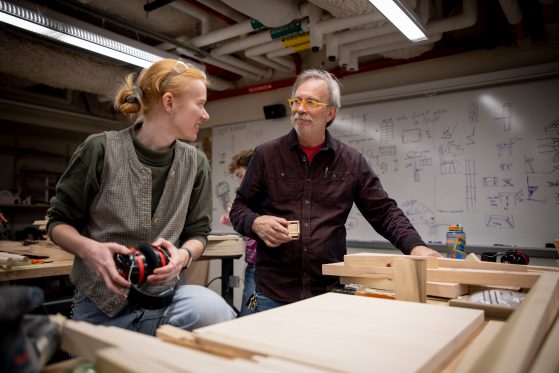 A man and woman stand over some wood material in a woodworking shop