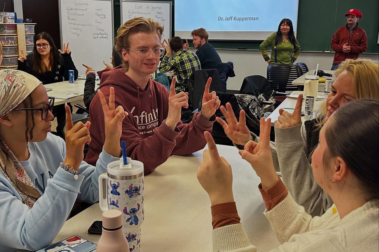 Nathan Malone sits at a table in a classroom with 3 other students. All 4 are holding up their fingers as part of a game.