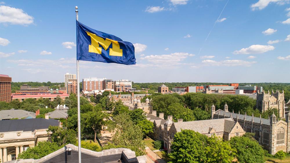 The campus skyline including a blue flag with the block-M logo on it.