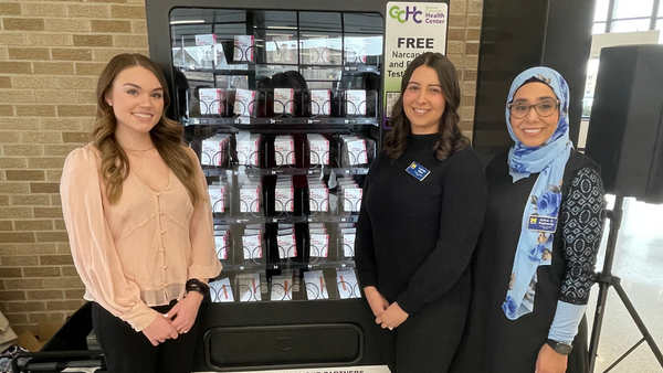 Three UM-Flint students standing in front of a NARCAN vending machine.
