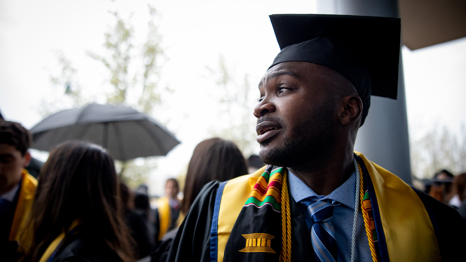 A young man in cap and gown with colorful cords and stole