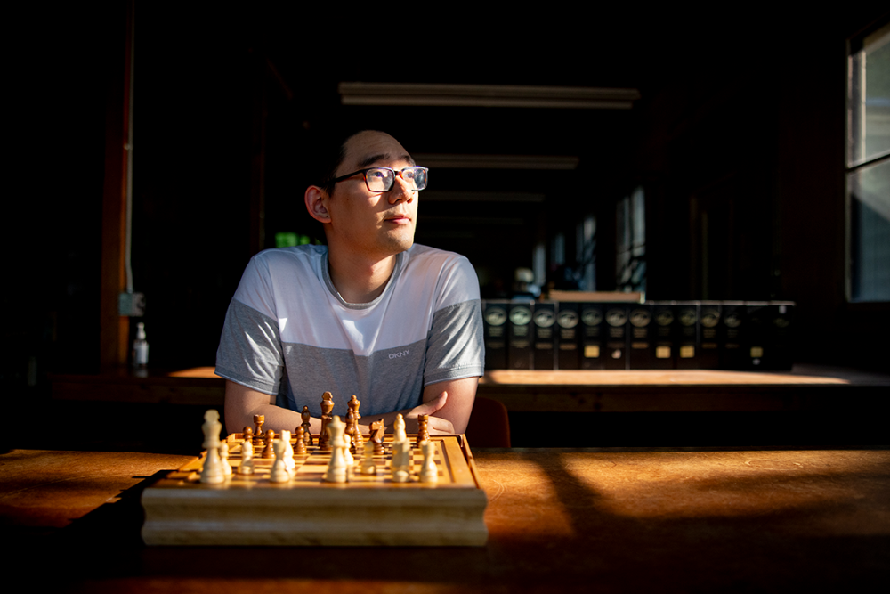 A person sitting in front of a chessboard is looking out the window.