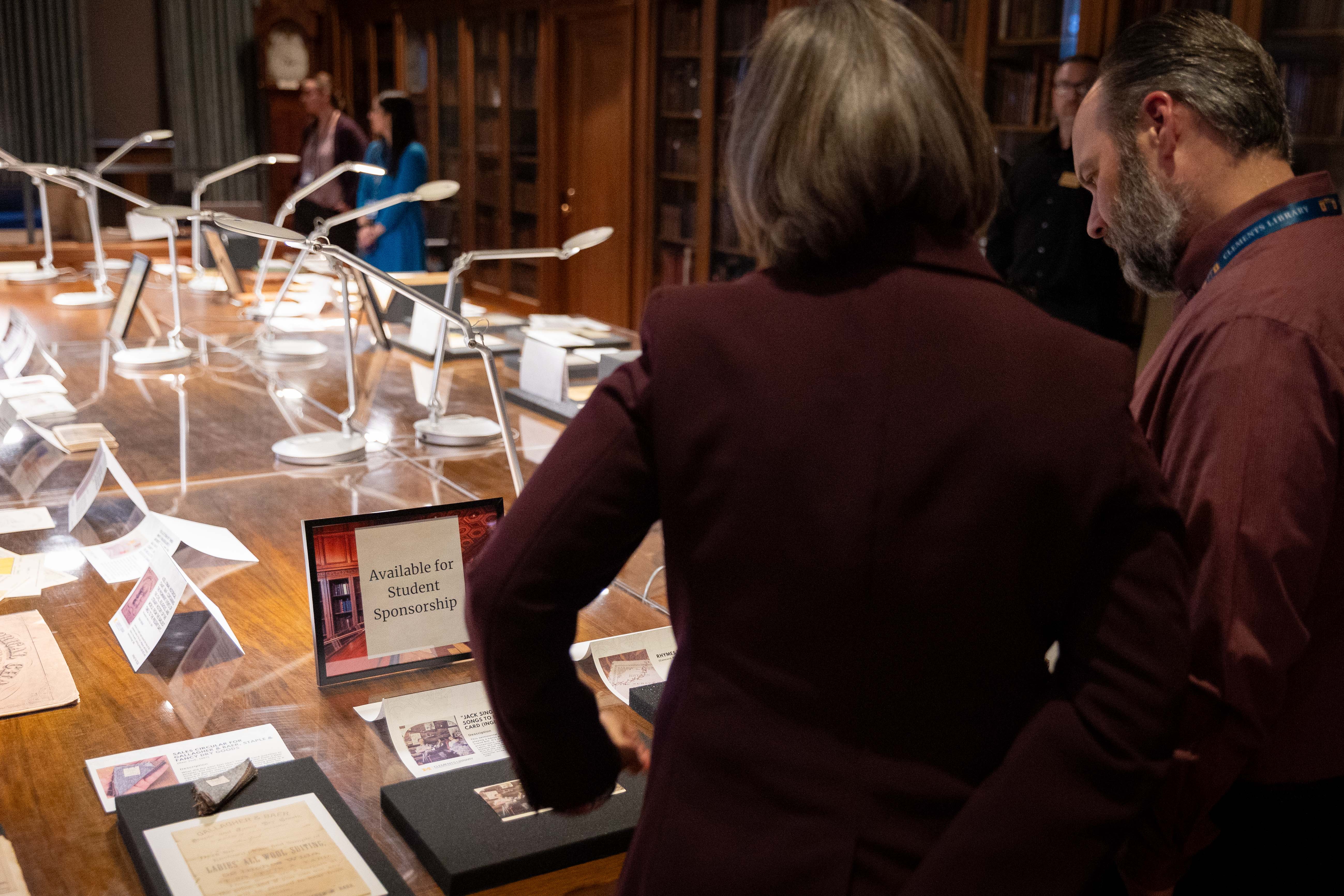 Two people looking at artifacts and a sign that reads 'Available for Student Sponsorship.'
