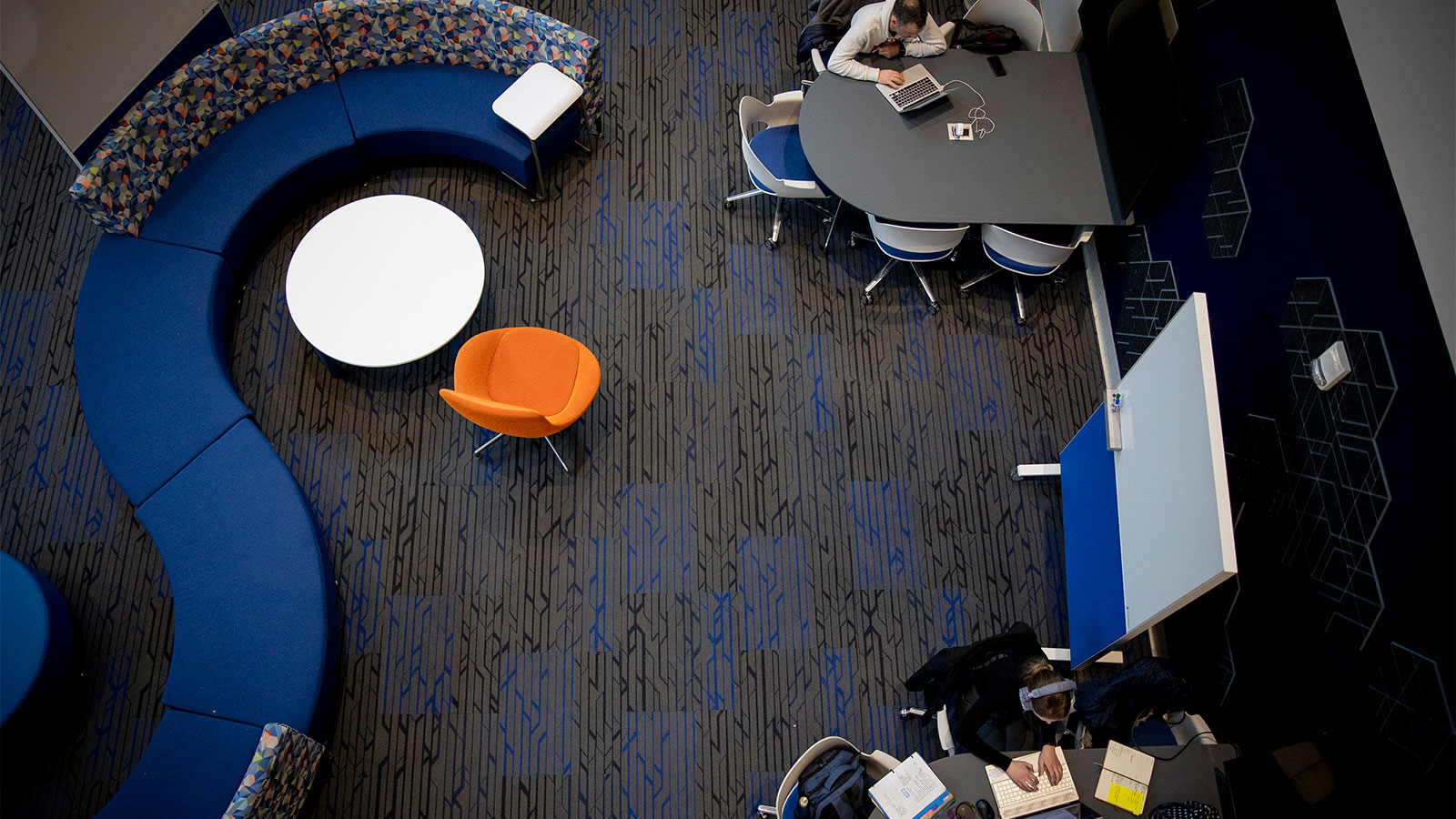 An overhead shot of an area with colorful tables, chairs, and students studying.