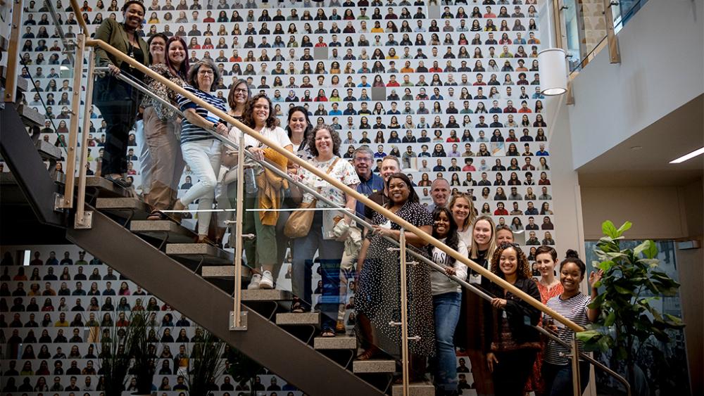 The team of people who make up the Office of Diversity, Equity, and Inclusion in the Office of University Development standing in front of a mosaic of portraits.