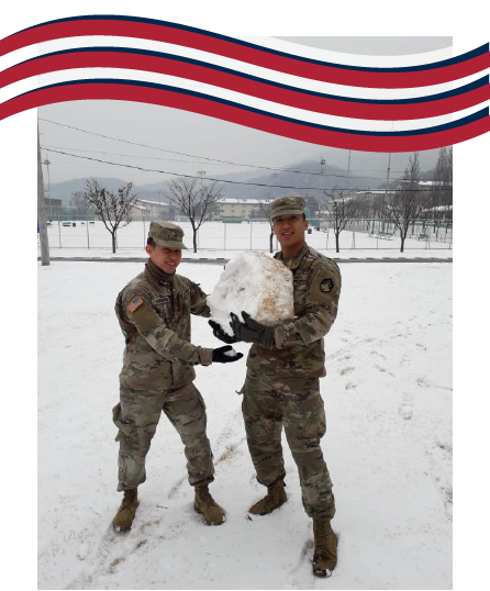 Arjan Goenaga Castillo and a member of his Army platoon standing in the snow and holding a large snowball while wearing their Army uniforms.