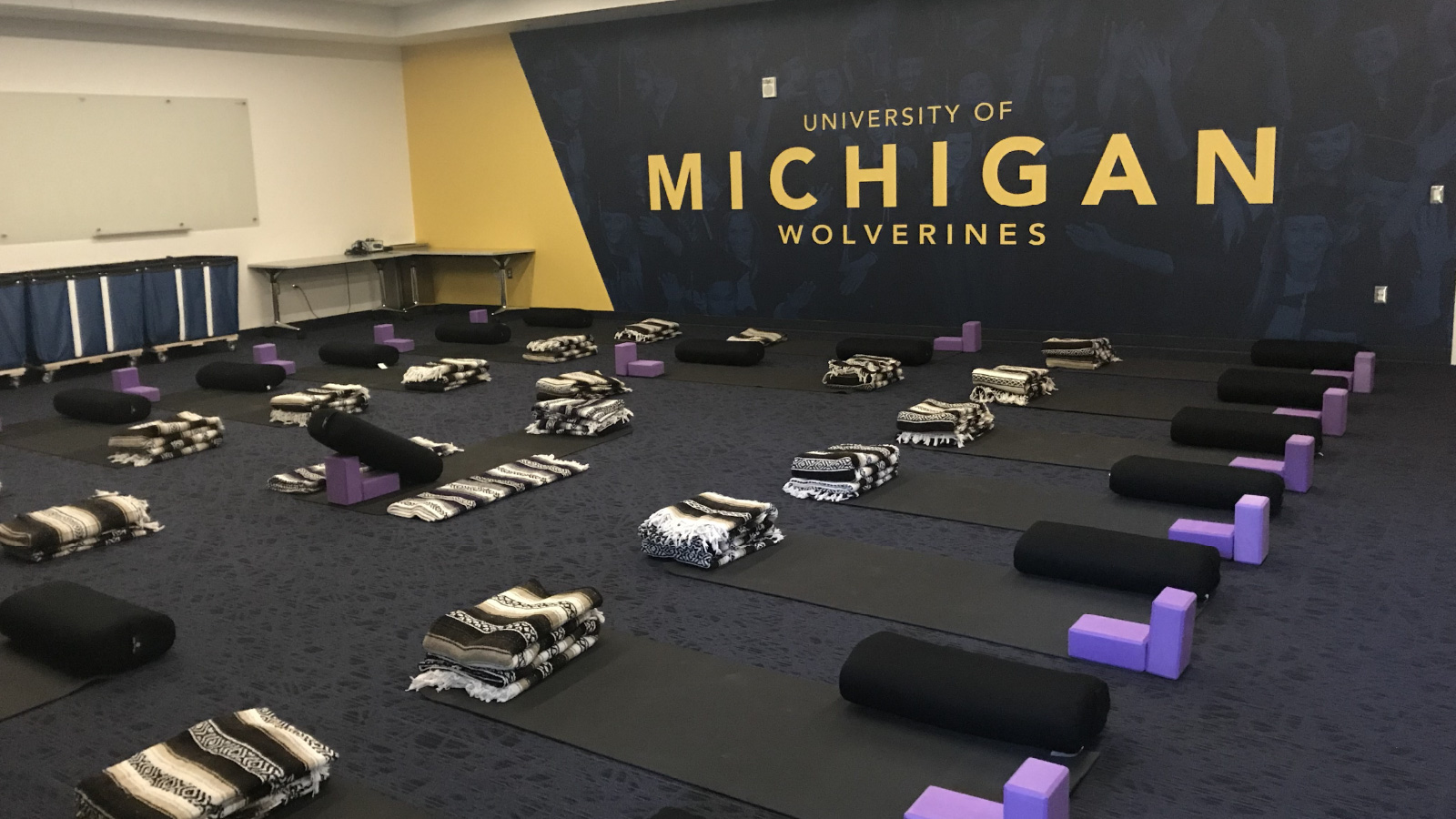 A room with yoga equipment. There’s a large sign on the wall that reads University of Michigan Wolverines.