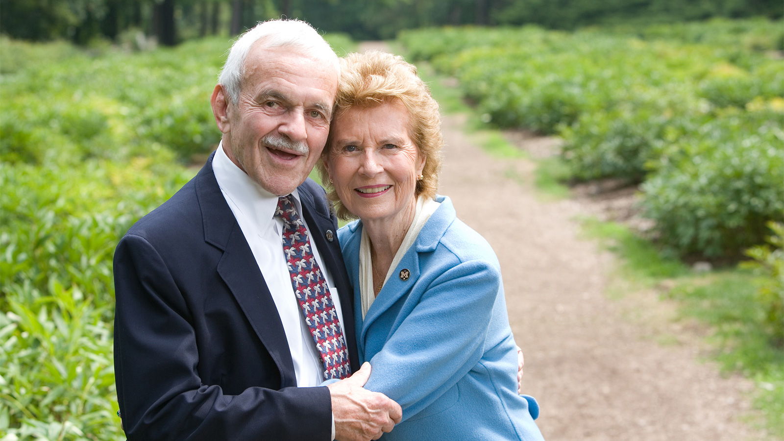 Fred and Barbara Erb wearing formal attire and embracing beside a garden path.